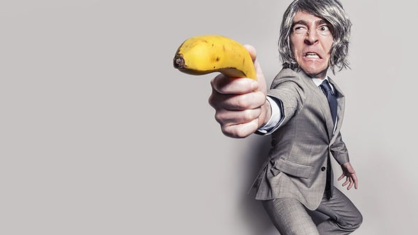 Lustiges Mann hält eine Banane als Waffe in der Hand